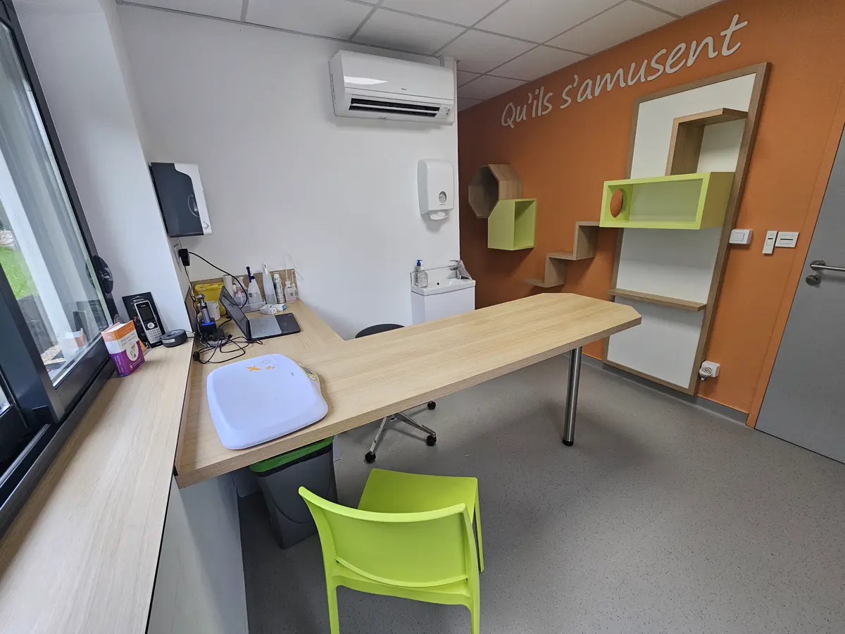 Salle de consultation au mur orange, avec l’inscription « Qu’ils s’amusent » et des étagères pour que les chats grimpent.